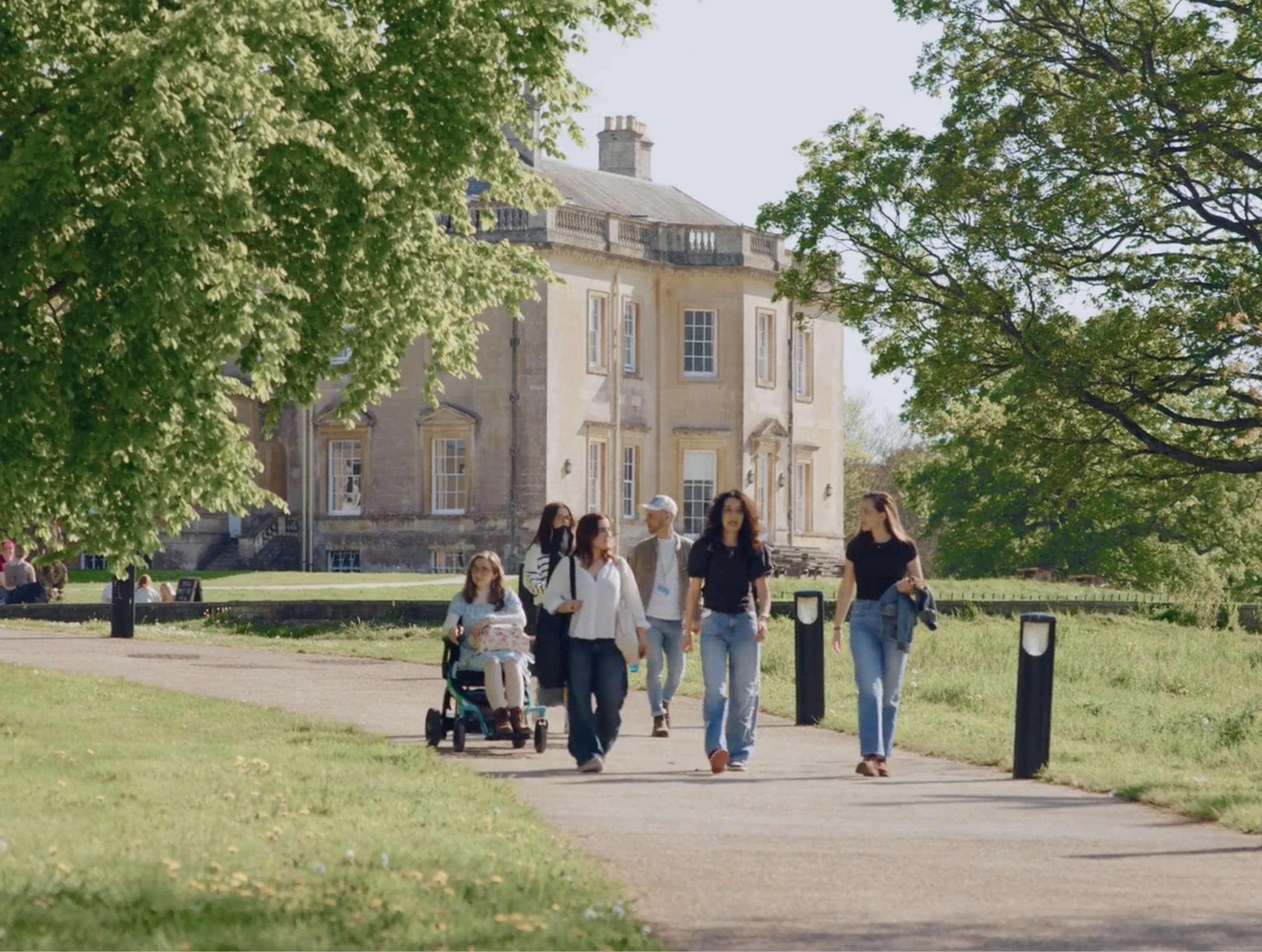 A group of students walk together along path in a park-like setting beside a large historic building.