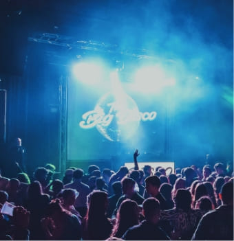 A crowd of people dances in a dark, smoky venue illuminated by bright blue and purple stage lights.
