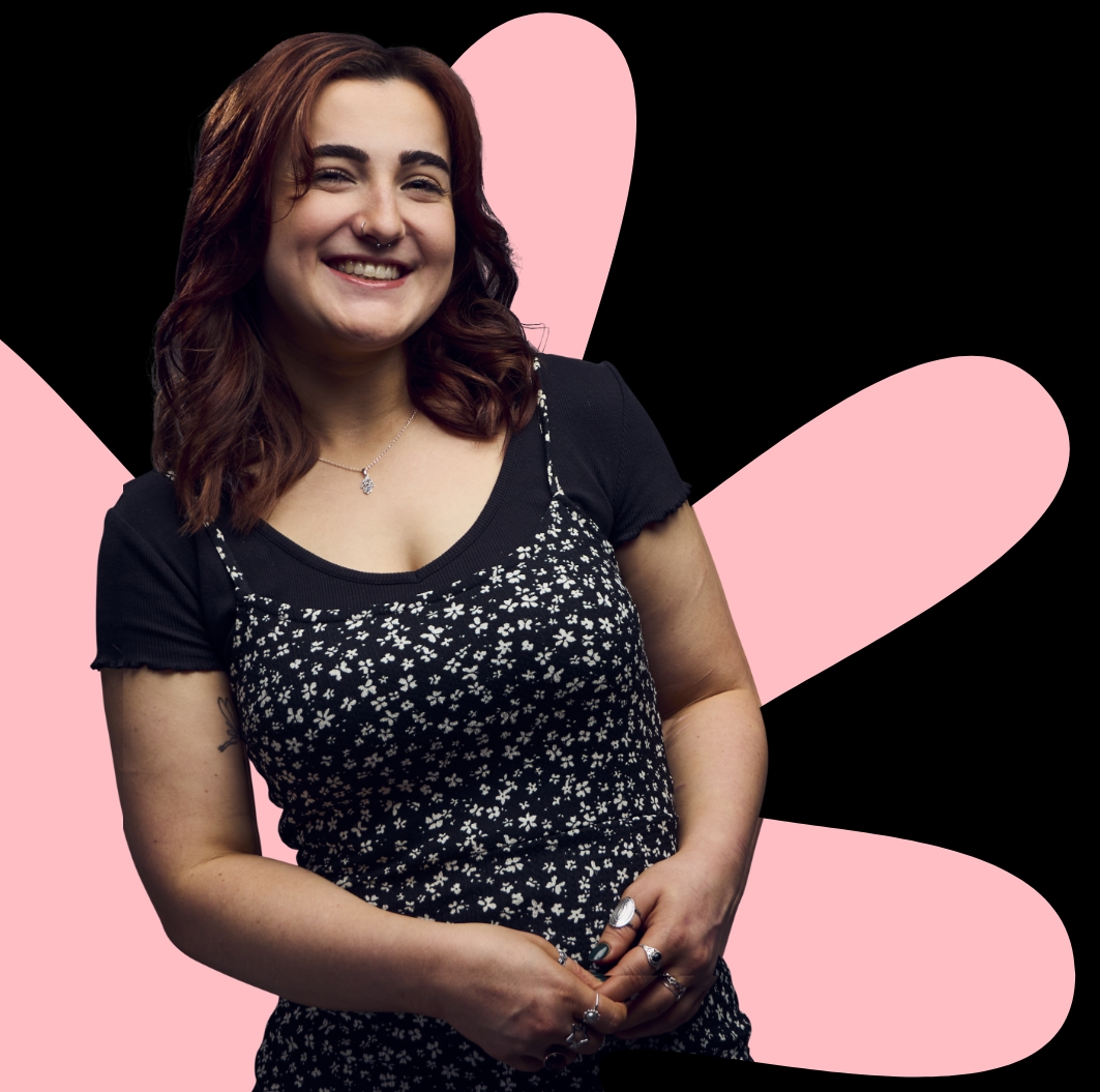 A person in dark clothing stands against a black background with large pink abstract shapes behind them.