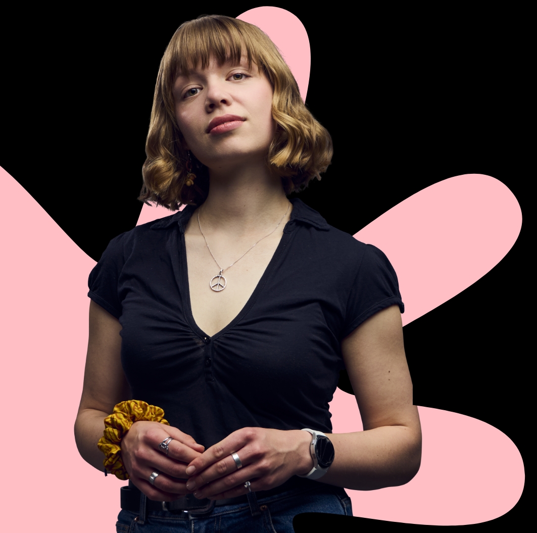 A person wearing dark clothing stands against a black background with large pink abstract shapes behind them.