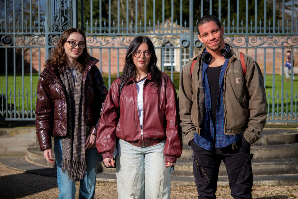 Three students facing the camera and stood in front of an ornate metal gate on Newton Park campus.